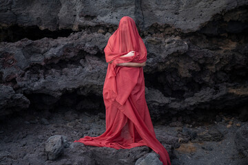 Young woman covered in a long red veil from had to toes looking up with the eyes closed while...