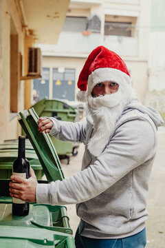 Papa Noel sin techo bebiendo vino y urgando en los contenedores de basura