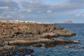 Fototapeta na wymiar Coastal scene with rocky shores and deep blue waters, near the rugged volcanic hiking path connecting the natural monument Montana Amarilla and Amarilla Golf resort in Tenerife, Canary Islands, Spain