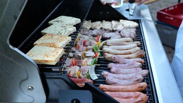 BBQ Close-up shot. Different types of steaks and sausages on a big barbeque grill. A sausage is getting turned on a grill. BBQ grill full stacked with meat and sausages. Delicious summer bbq food. 