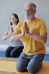 man and woman do yoga in sports studio. senior coach and young adult female meditate with their eyes closed. lotus pose and namaste hands. relaxation, relaxation practices, health care