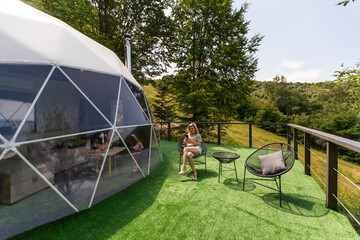 A woman sits in a geo dome glamping tent, looks at the nature.