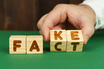 On a green surface, a man puts cubes with the inscription - FAKE, FACT