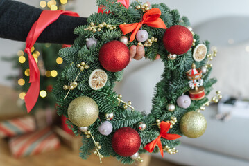 Unrecognizable female hand holds a Christmas wreath beautifully decorated with red ornaments.