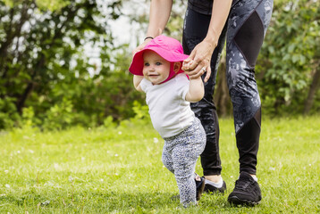 A mother teaching her baby girl to walk on a warm summer day in a city park; Edmonton, Alberta, Canada