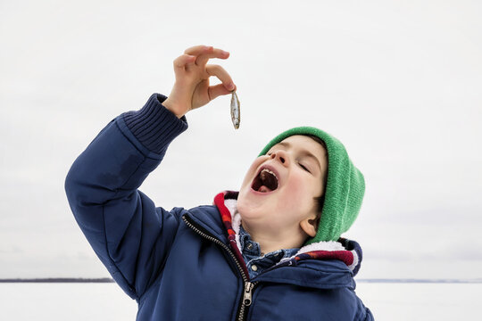 Young boy pretending to eat a baitfish minnow while ice fishing at Wabamun Lake; Wabamun, Alberta Canada