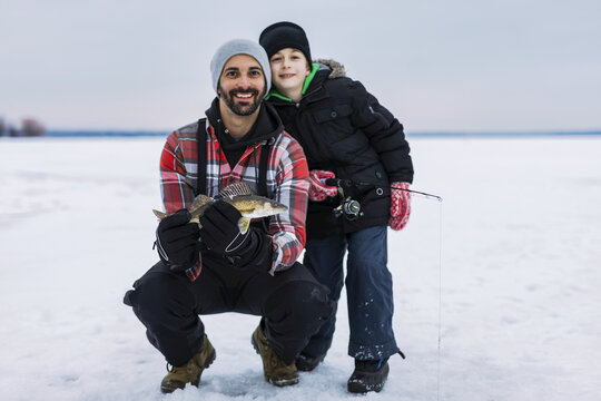 Father and young son showing off their catch of a walleye before releasing it while ice fishing at Lake Wabamun; Wabamun, Alberta, Canada