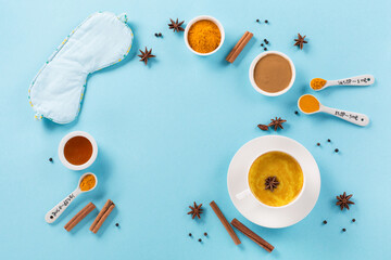 Turmeric golden milk latte with spices, cinnamon, honey and Sleep mask on blue background.