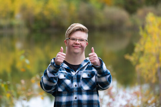 A young man with Down Syndrome giving a thumbs up in a city park on a warm fall evening: Edmonton, Alberta, Canada