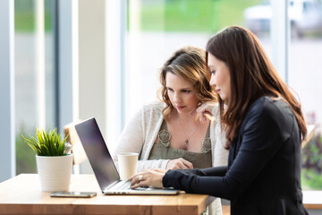 Two professional business woman working together on a computer in a coffee shop: Edmonton, Alberta, Canada