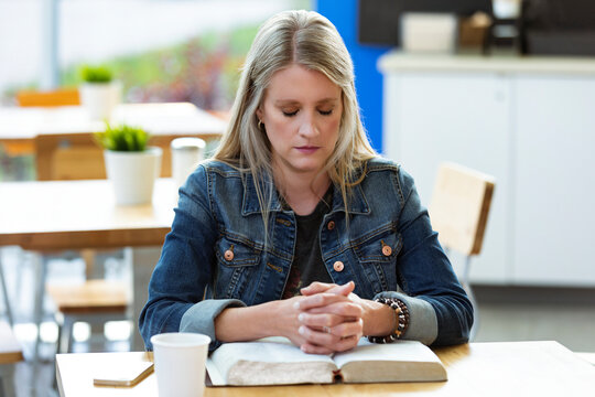A mature woman praying, after doing some personal Bible study, in a coffee shop; Edmonton, Alberta, Canada