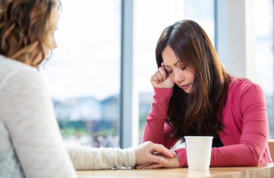 A mature Christian woman mentoring and praying with a young woman during a bible study in a coffee shop at a church: Edmonton, Alberta, Canada