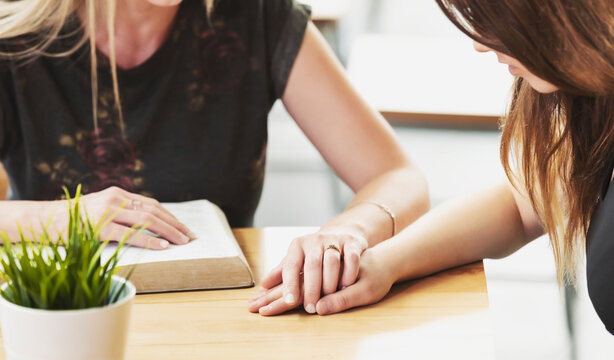 A mature Christian woman mentoring and praying with a young woman during a bible study in a coffee shop at a church: Edmonton, Alberta, Canada