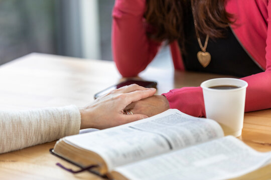 A mature Christian woman mentoring and praying with a young woman during a bible study in a coffee shop at a church: Edmonton, Alberta, Canada