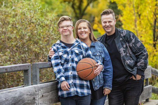 A young man with Down Syndrome with his father and mother while enjoying each other's company in a city park on a warm fall evening; Edmonton, Alberta, Canada