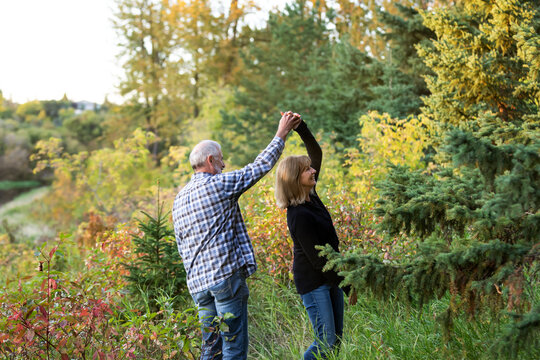 A mature couple enjoying quality time and dancing together while walking along a river in a city park on a warm fall evening; St. Albert, Alberta, Canada