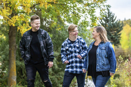 A young man with Down Syndrome walking with his father and mother while enjoying each other's company in a city park on a warm fall evening; Edmonton, Alberta, Canada