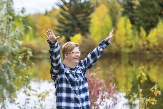 A young man with Down Syndrome raising his hands in worship to God, while in a city park on a warm fall evening; Edmonton, Alberta, Canada
