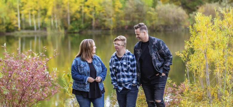A young man with Down Syndrome walking with his father and mother while enjoying each other's company in a city park on a warm fall evening; Edmonton, Alberta, Canada