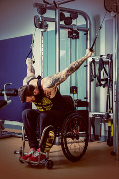 A paraplegic man working out using a crossover pulley weight lifting apparatus in a fitness facility; Sherwood Park, Alberta, Canada