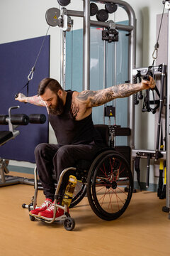 A paraplegic man working out using a crossover pulley weight lifting apparatus in a fitness facility; Sherwood Park, Alberta, Canada