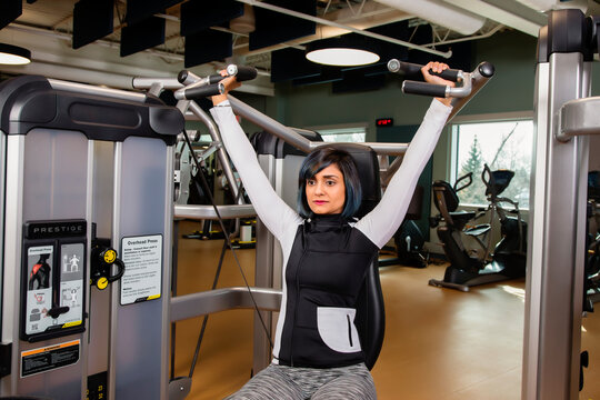 A paraplegic woman working out using an overhead press in a fitness facility; Sherwood Park, Alberta, Canada