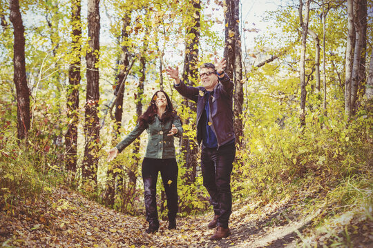 Mature couple throwing autumn leaves in the air and enjoying each other's company while taking a walk in the woods; St Albert, Alberta, Canada