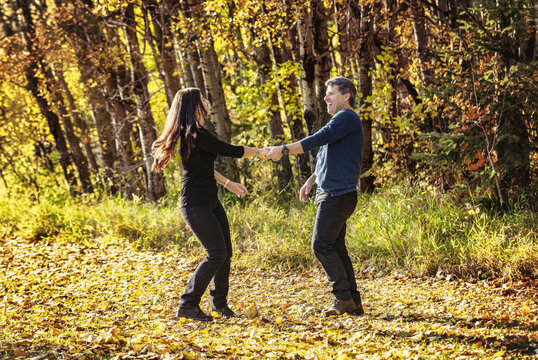 Mature couple dancing in the autumn leaves and enjoying each other's company while taking a walk in the woods; St Albert, Alberta, Canada