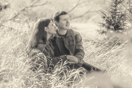Portrait of mature couple sitting in the tall grass holding hands and enjoying nature while on a walk in the woods in autumn; St Albert, Alberta, Canada