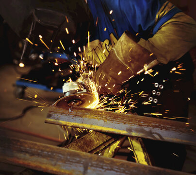 Tradesman grinding a steel beam in a metal fabrication plant; Innisfail, Alberta, Canada