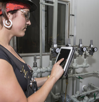 Female trades worker using a tablet while programming instrumentation; Innisfail, Alberta, Canada