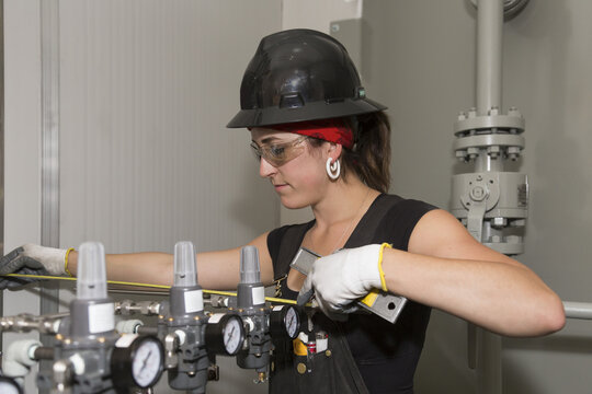 Female trades worker uses a measuring tape to install the fuel gas regulator; Innisfail, Alberta, Canada