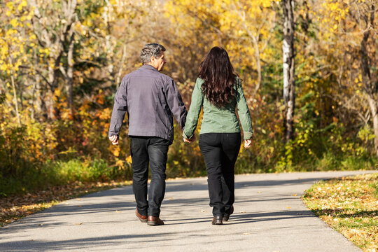 A mature married couple walking together and holding hands in a park during the fall season; St. Albert, Alberta, Canada
