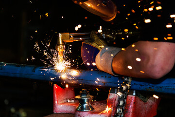 A journeyman pipe fitter in a metal fabrication plant using an Acetylene torch to cut a hole in a pipe to prepare it for a joint to another pipe; Innisfail, Alberta, Canada