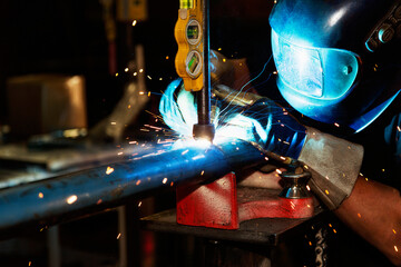 A journeyman pipe fitter in a metal fabrication plant using an Acetylene torch to cut a hole in a pipe to prepare it for a joint to another pipe; Innisfail, Alberta, Canada