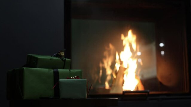 Christmas present, room interior celebration concept. Christmas tree branch with colorful balls, two gift boxes with golden ribbons, burning fireplace background. Warm family moments.
