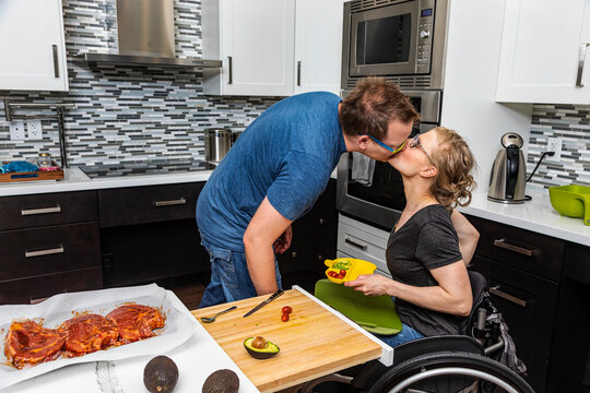 A paraplegic woman preparing a meal for her family in her kitchen while working from a wheelchair when her husband kisses her; Edmonton, Alberta, Canada