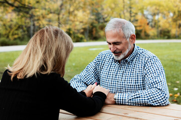 A mature couple praying together at a picnic table on a warm fall day in a city park; St. Albert, Alberta, Canada