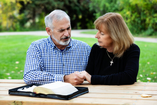A mature couple praying together at a picnic table after spending some quality time discussing their faith; St. Albert, Alberta, Canada