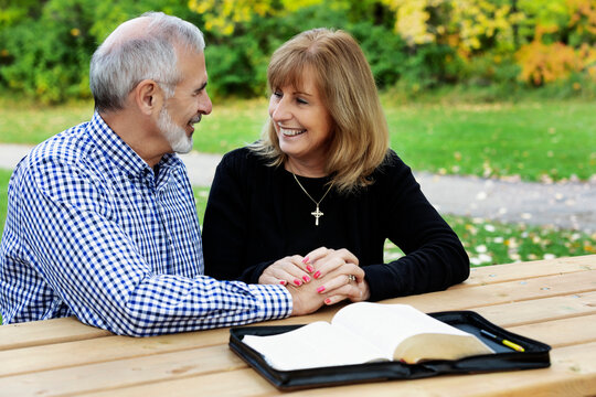A mature couple sharing devotional time together and studying the bible at a picnic table on a warm fall day in a city park; St. Albert, Alberta, Canada