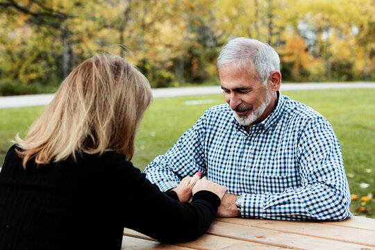 A mature couple praying together at a picnic table on a warm fall day in a city park; St. Albert, Alberta, Canada