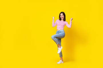Fototapeta na wymiar Full size photo of winsome young girl raise fists celebrate achieve goal dressed trendy striped clothes isolated on yellow color background