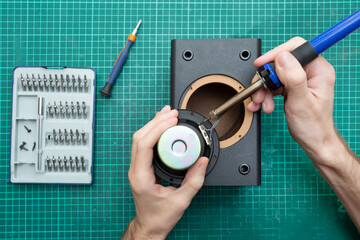 The master holds a soldering iron while repairing an audio speaker. Musical speaker repair service....