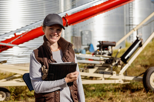 Cropped portrait of a female farmer smiling cheerfully while holding a digital tablet and standing on a modern farm; Alcomdale, Alberta, Canada