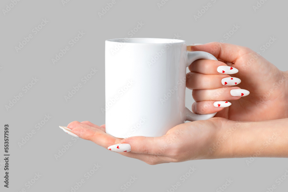 Wall mural women's hands hold a mockup of a white empty mug on a gray background, a cup for your design and log