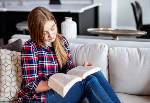 Teenage girl sitting on a couch at home and reading the Bible; Edmonton, Alberta, Canada