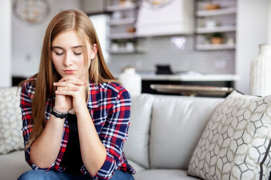 Teenage girl sitting on a couch at home and spending time in prayer; Edmonton, Alberta, Canada