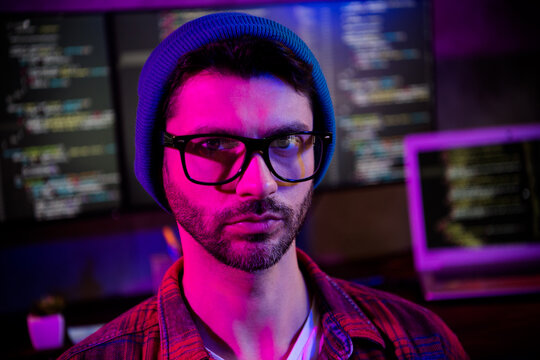 Photo of confident serious freelancer wear hat eyeglasses coding java script website indoors workplace workstation loft