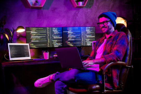 Photo of positive happy coder dressed hat eyewear typing modern device indoors workplace workstation loft