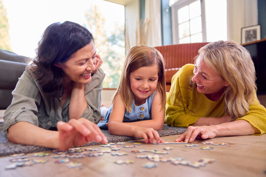Same Sex Family With Two Mature Mums And Daughter Lying On Floor Doing Jigsaw Puzzle At Home